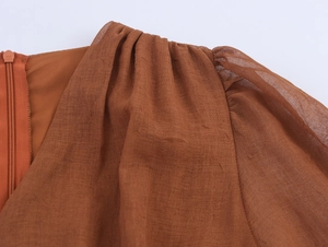 Detail view of caramel V-neck dress showing shoulder pleats and invisible back zipper