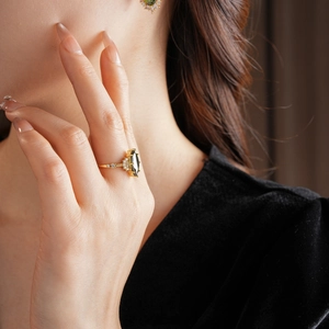 Dettaglio di un anello dorato con gemma marquise verde oliva e orecchini coordinati