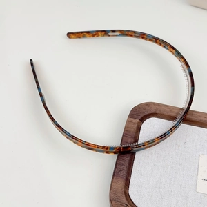 Détail d'un serre-tête en acétate écaille de tortue avec motifs bleus sur support bois