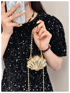 Detail of a mini golden shell-shaped metal handbag with elegant chain strap on a model