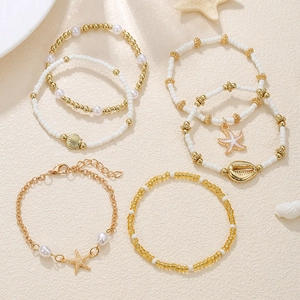 Detail of gold starfish and shell beaded bracelets set on white textured surface