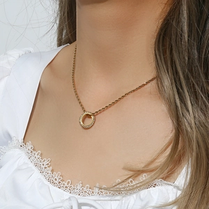 Detail of a golden twisted chain necklace with a sparkling zircon ring pendant on a model