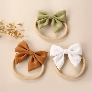 Detailed view of three soft nylon baby headbands with bows in green, brown, and white colors