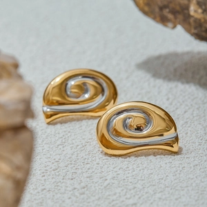 Dettaglio di orecchini a spirale bicolore oro e argento con finitura metallica minimalista