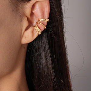 Detail view of a 3-piece set of golden irregular geometric metal ear cuffs on a model ear