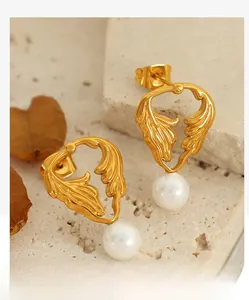 Detailed view of gold leaf stud earrings with white pearl drops on elegant stone texture
