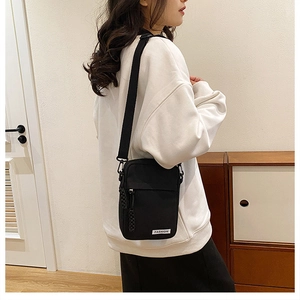 Detail of a black mini canvas crossbody bag with Fashion label worn by a model