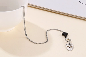 Detail of skull pendant and black cross on steel chain with OT clasp over beige background