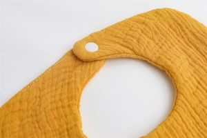 Close-up of yellow multi-layer muslin cotton baby bib showing snap button and soft fabric