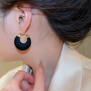 Close-up of elegant black flocked U-shaped earrings with gold metal accents on a model