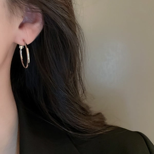 Close-up of a silver geometric hoop earring worn by a model in black attire