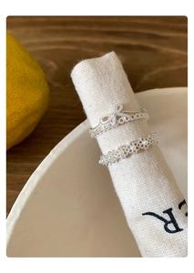 Detailed view of silver bow and pearl open rings set against a rustic linen backdrop