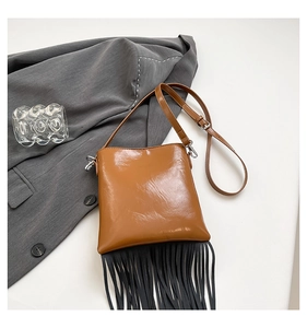 Detail of a brown glossy crossbody bag with long black fringe and silver metal accents