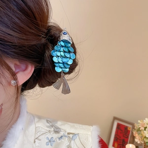Detailed view of a silver fish hair clip with blue scales on hair bun for women