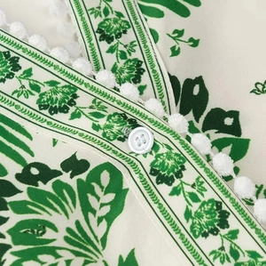 Macro detail of the V-neckline with pom-pom trim and white button on floral maxi dress