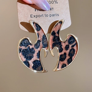 Macro shot of geometric gold earrings featuring leopard print leather and flame arc design