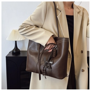 Close-up of brown oversized tote bag with white contrast stitching and cat charm