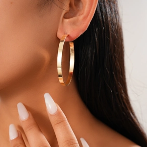 Close-up of model wearing a large minimalist metallic gold geometric hoop earring