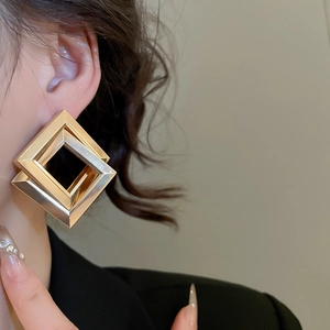 Macro shot of oversized geometric square earrings with matte gold and silver metal finish
