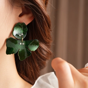 Detail of dark green leaf-shaped resin earrings with small rhinestones on model