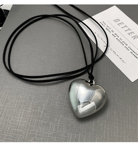 Detailed view of a polished silver heart pendant on a black cord necklace over gray texture