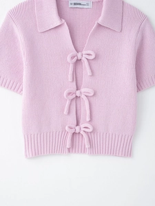Close-up of pink knit top featuring delicate bow ties and a refined polo collar detail