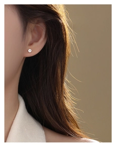 Detailed view of silver cross screw stud earring worn on ear with polished finish