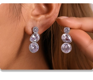 Close-up of triple zircon drop earrings in silver finish worn by a fashion model