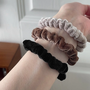 Detailed texture of three velvet scrunchies in black, dark brown, and silver grey colors