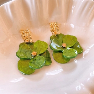 Detail of green four-leaf clover earrings with golden hammered texture studs in a bowl