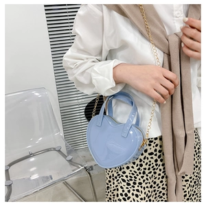 Detail view of a light blue heart-shaped jelly bag with gold chain strap worn by a model