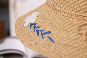 Close-up of raffia sun hat featuring blue wavy stitching and a white daisy flower detail
