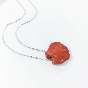 Close-up of irregular reddish natural stone pendant with silver chain over white background