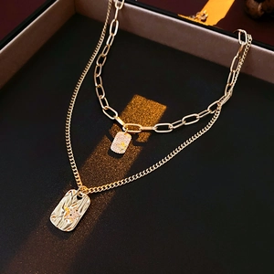 Close-up of golden double-layer necklace with a diamond-set square and a textured pendant