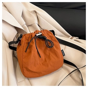 Detail of orange drawstring bucket bag with black strap on a beige trench coat