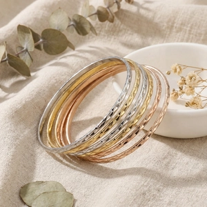 Macro view of stacked diamond-pattern titanium steel bracelets in silver, gold, and rose gold