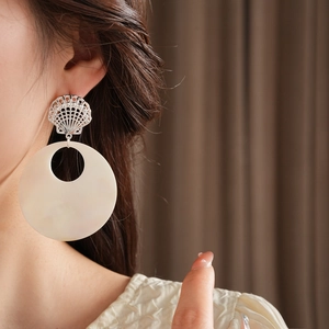 Close-up of oversized circular white drop earrings with silver seashell detail on model