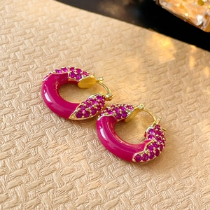 Vue macro de boucles d'oreilles créoles C en émail rose rouge avec détails en zircon