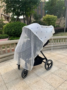 Close-up of baby stroller with white floral mosquito net and patterned windproof cover