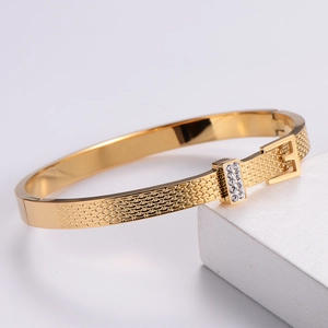 Elegant gold metal bracelet with crystal inlay and buckle design on a white pedestal