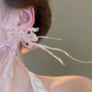 Macro shot of pink beaded bow earrings with feathers worn by a model in warm light
