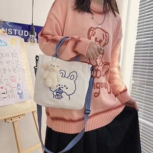 Detail of canvas tote bag with cartoon bunny print, blue straps and plush bear charm
