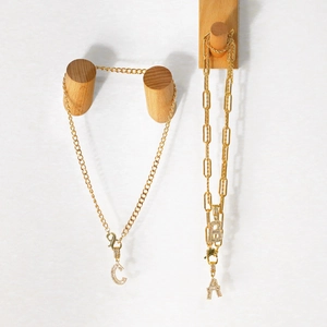 Detail of gold zircon initial necklaces on wood hooks showing delicate chains and craftsmanship