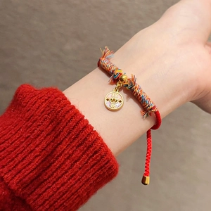 Détail d'un bracelet en corde tressée rouge avec un pendentif porte-bonheur doré