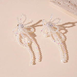 Detail of sweet crystal bow earrings with long tassels on a soft pink background