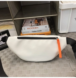 Detail of white crossbody bag with black zipper and orange puller on textured surface