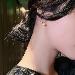 Detailed close-up of crystal bow stud earring with white pearls on ear model