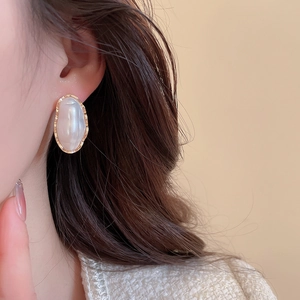 Close-up of elegant oval pearl earrings with golden wavy frames on model