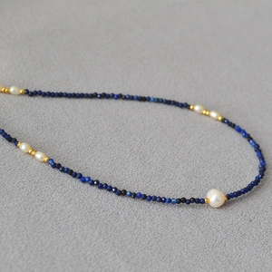 Lapis lazuli beaded necklace with freshwater pearls and gold accents on gray fabric