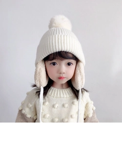Detail of warm off-white knit winter hat for kids with soft pompom and ear protection flaps